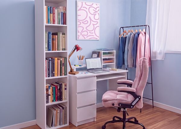 Moderne studieplads til studerende med et hvidt skrivebord, ergonomisk kontorstol, laptop, bogreol, opbevaringsm&oslash;bel og t&oslash;jstativ i et lyst og organiseret sovev&aelig;relse, der er indrettet til behagelig l&aelig;sning og hverdagen som studerende.