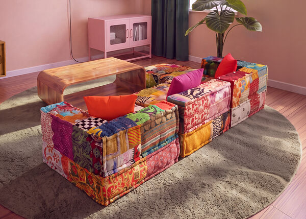 Farverig modulsofa i patchwork opstillet rundt om et sofabord i tr&aelig; p&aring; et rundt t&aelig;ppe i en moderne stue.