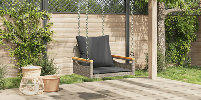 Udendørs gyngebænk i rattan med mørke hynder på en terrasse. Klik for at købe kollektionen.
