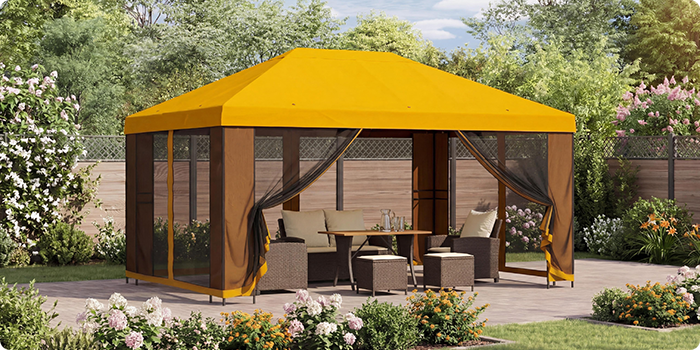 Gul havepavillon med netgardiner, der dækker et loungesæt med bord på en terrasse omgivet af blomstrende planter i en solrig have.